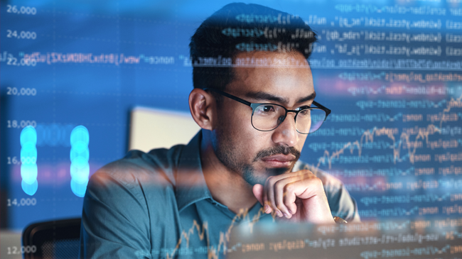 A person wearing glasses and a blue shirt sits in front of a computer screen displaying complex code and financial data overlays. The blue background features bar charts and numerical graphs, indicating a focus on data analysis or programming. The person appears thoughtful and concentrated.